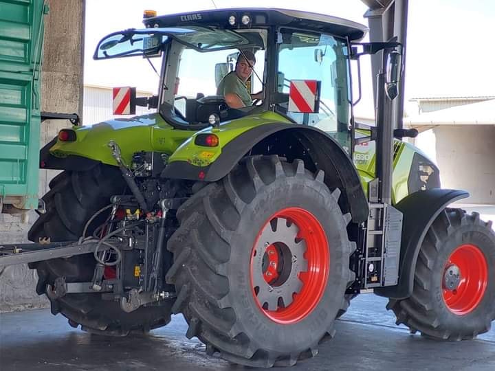 Egy gazdálkodó, aki egy nagyméretű zöld és piros traktort üzemeltet, túlméretezett gumikkal, egy garázsban, a vezetőülésből néz ki.