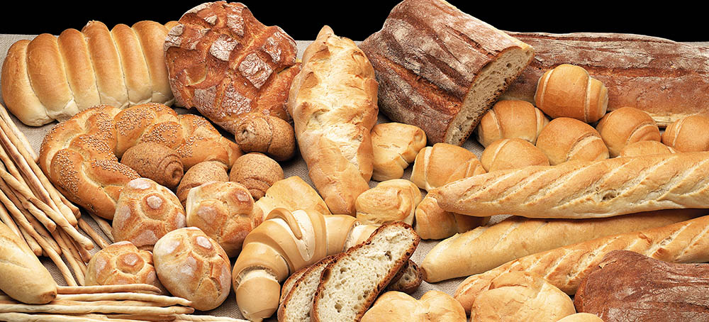 Különféle frissen sült kenyérfélék választéka, beleértve a bagetteket, zsemlét, cipókat és pereceket fa felületen.