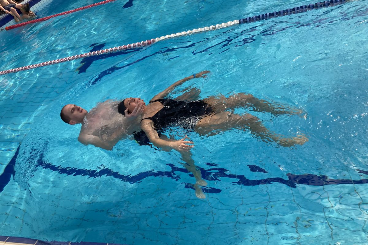 Egy személy, aki a hátán lebeg egy kék vizű medencében, sávelválasztókkal körülvéve.