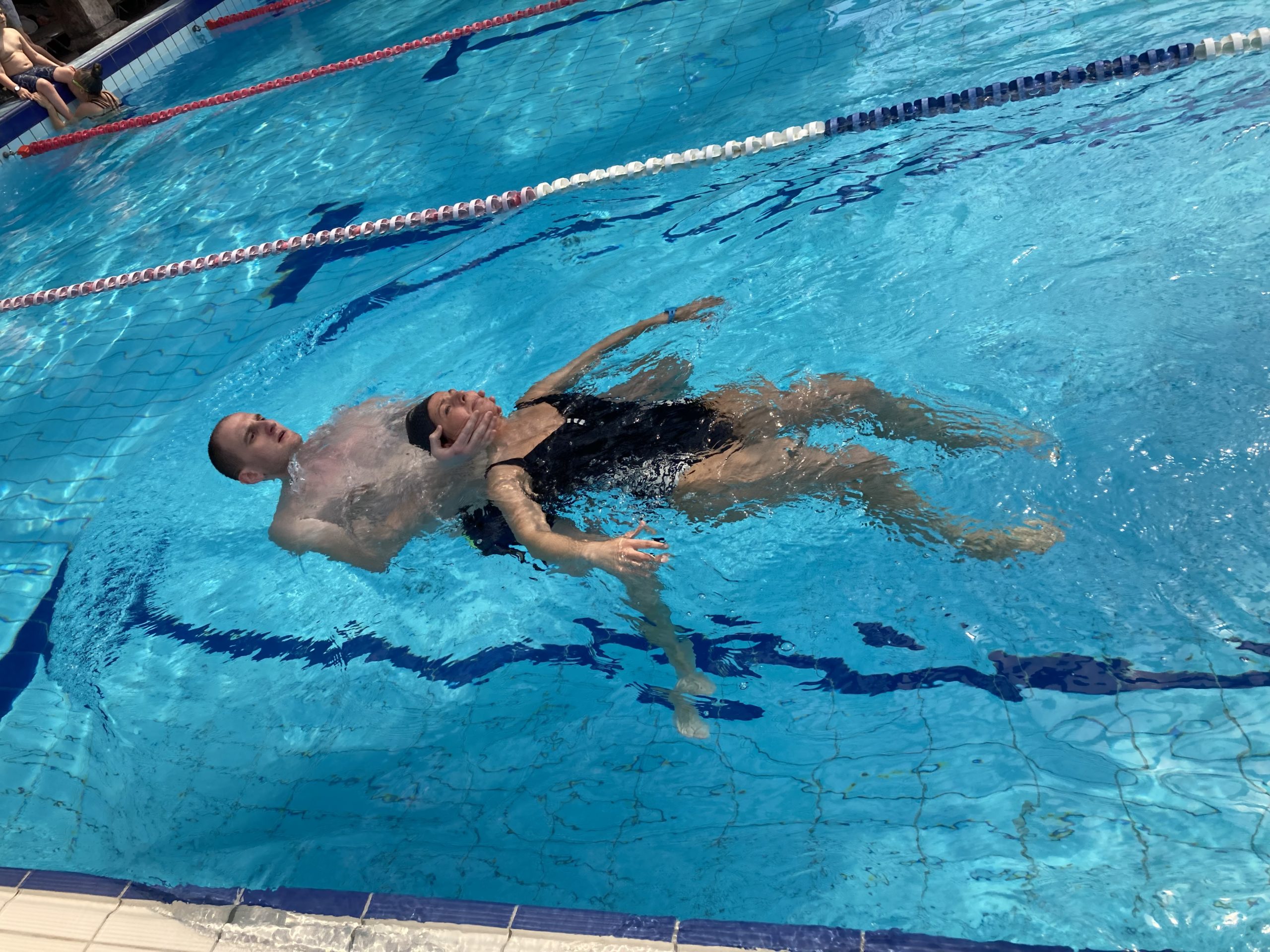 Egy személy, aki a hátán lebeg egy kék vizű medencében, sávelválasztókkal körülvéve.