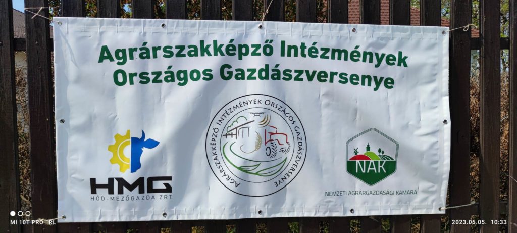 Fémkerítésre szerelt vízszintes fehér transzparens három magyar mezőgazdasági szervezet logójával és a mezőgazdasági intézmények országos pályázatát hirdető szöveggel.