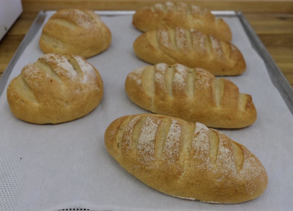 Sütőpapírral bélelt tepsiben frissen sült kenyerek aranyszínű kéreggel és karcolt tetejükkel.