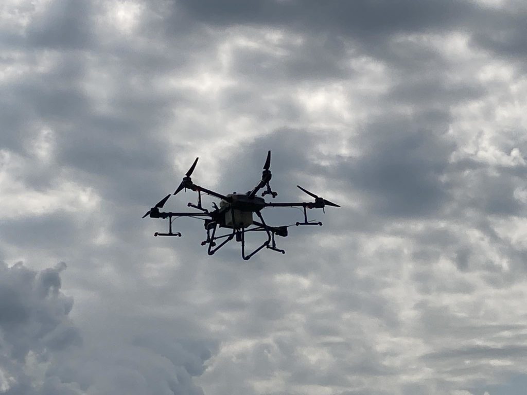 Egy drón több légcsavarral repül a felhős égen. A drón sziluettje jól látszik a szürke felhőkön, ami borult időre utal.