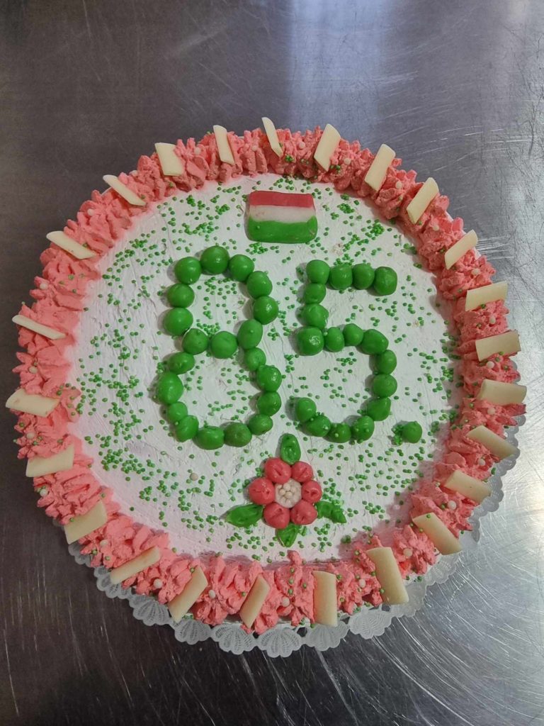 Kerek torta, a tetejére zöld cukormázzal a "85" szám van írva. A tortát a szélein rózsaszín és fehér cukormáz díszíti, tetején egy kis magyar zászló. Zöld fröccsök, piros és rózsaszín cukormázvirág, valamint fehér csokoládédarabok is díszítik a tortát.