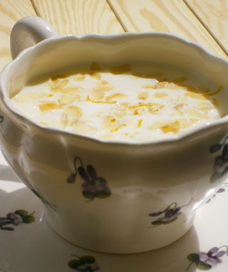 Egy hozzáillő csészealjra egy virágmintás csészét, tejszínes kukoricalevessel töltjük meg, mindkettőt apró ibolyavirágok díszítik. A levesben látható kukoricaszemek vannak, és úgy tűnik, hogy egy világos fából készült asztalon van.