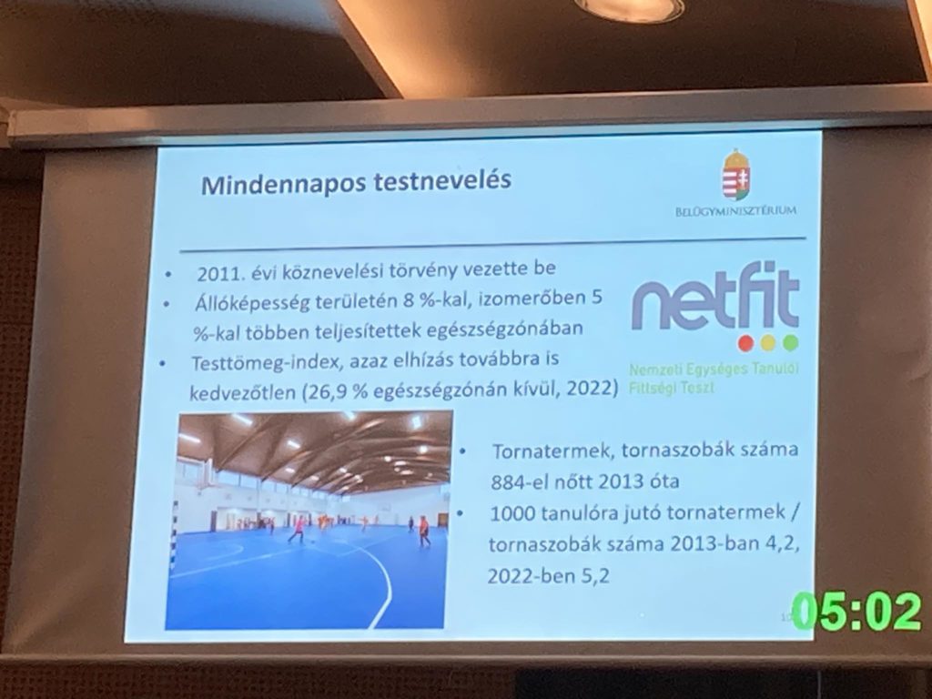 Prezentációs dia "Mindennapos testnevelés" címmel szöveggel és képekkel. A szöveg a testnevelés statisztikáit tárgyalja, beleértve egy 2011-es törvény hatását is. Van egy kép a diákokról egy tornateremben és logók. Az időbélyeg 05:02.