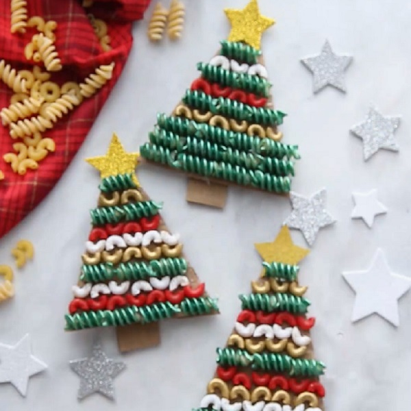 Három tésztából készült karácsonyfa alakú kézműves, zöld, piros és fehér váltakozó színekkel díszítve, felül csillaggal, alul fatörzsrel. Ezüst és fehér csillagdíszek veszik körül a fákat, a közelben piros ruhán főtt tészta.