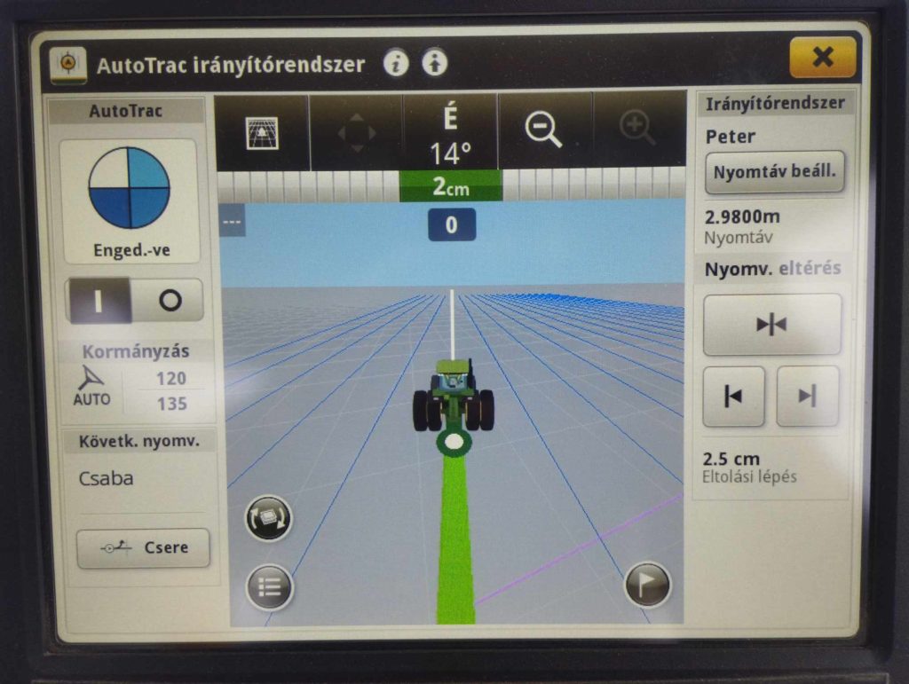 Közeli kép egy traktor AutoTrac vezetőrendszer képernyőjéről, amely különféle kezelőszerveket és beállításokat jelenít meg. A traktor útját felülről lefelé nézheti, és egy zöld vonal jelzi az irányt. A címkék és a szöveg magyar nyelvű, olyan paramétereket mutatva, mint a távolság és a szögeltérés.