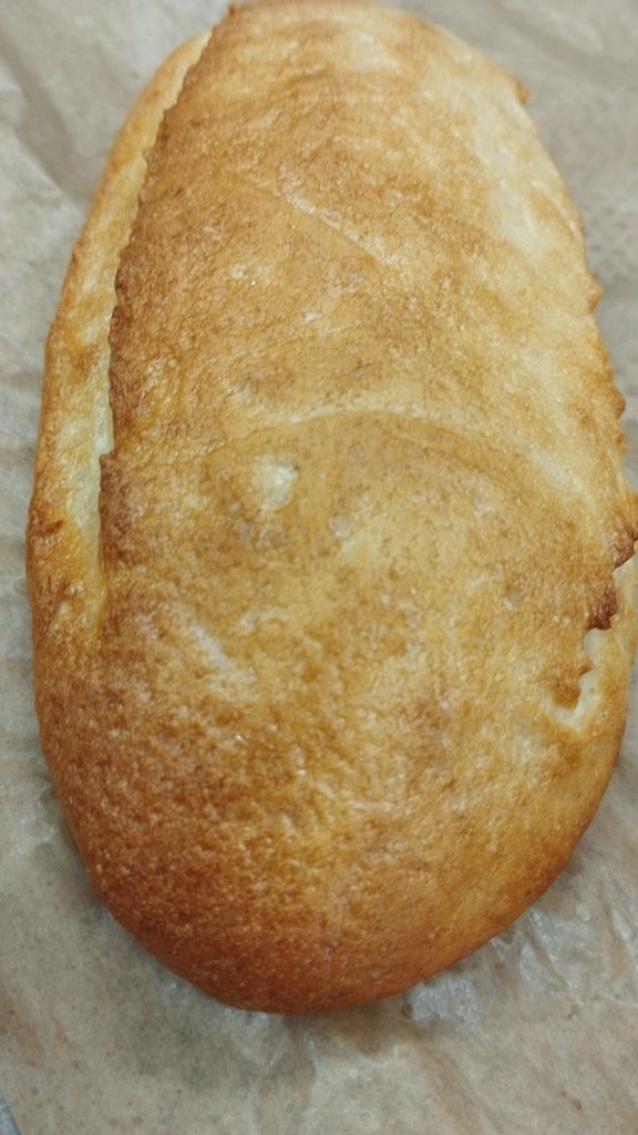 Közeli kép egy aranybarna kenyérről, amely sütőpapíron pihen. A kenyér texturált kéreggel rendelkezik, és frissen sültnek tűnik.