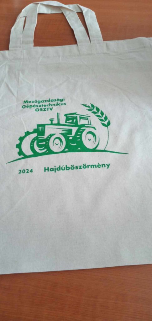 Bézs színű táska zöld szöveggel és grafikával. Egy traktort és búzaszárat ábrázol. Felül magyar szöveg „Mezőgazdasági Gépésztechnikus”, a traktorgrafika alatt „2024” és „Hajdúböszörmény” olvasható.